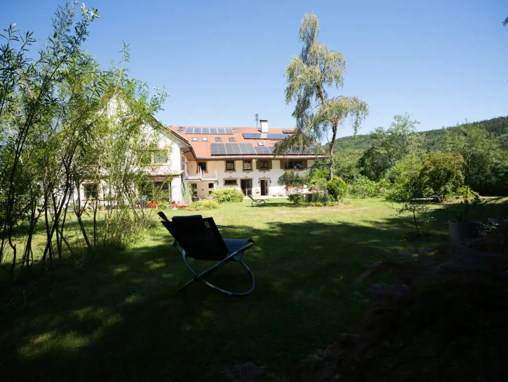 Liegestuhl im Garten unter Bäumen mit Blick auf das Haus
