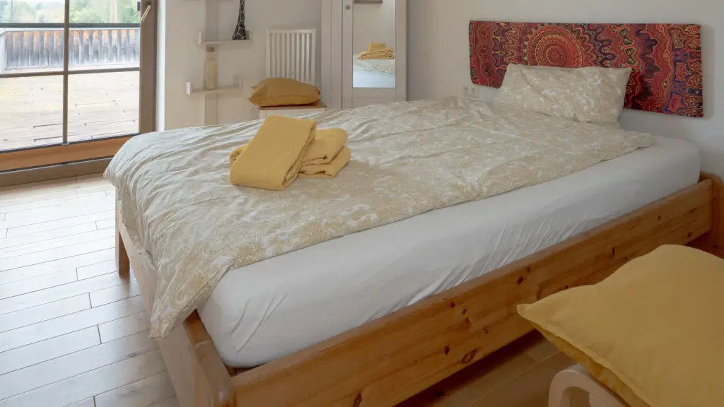 Zimmer 1: Einzelbett aus Holz mit farbenfrohem Kopfteil vor einem großen Fenster