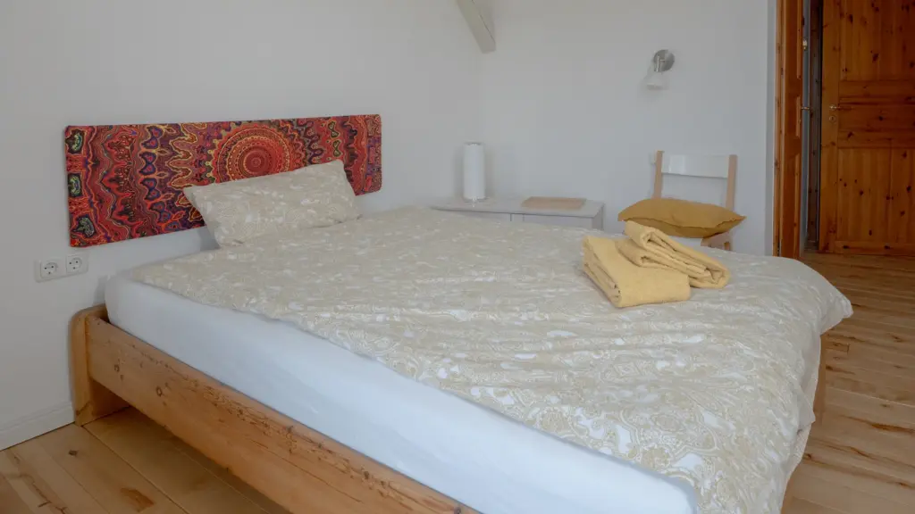 Zimmer 1: Holzbett mit gelber Bettwäsche, daneben eine Tür aus Kiefernholz