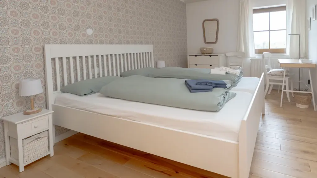 Zimmer 2: weißes Doppelbett vor gemusterter Tapete, Schreibtisch am Fenster
